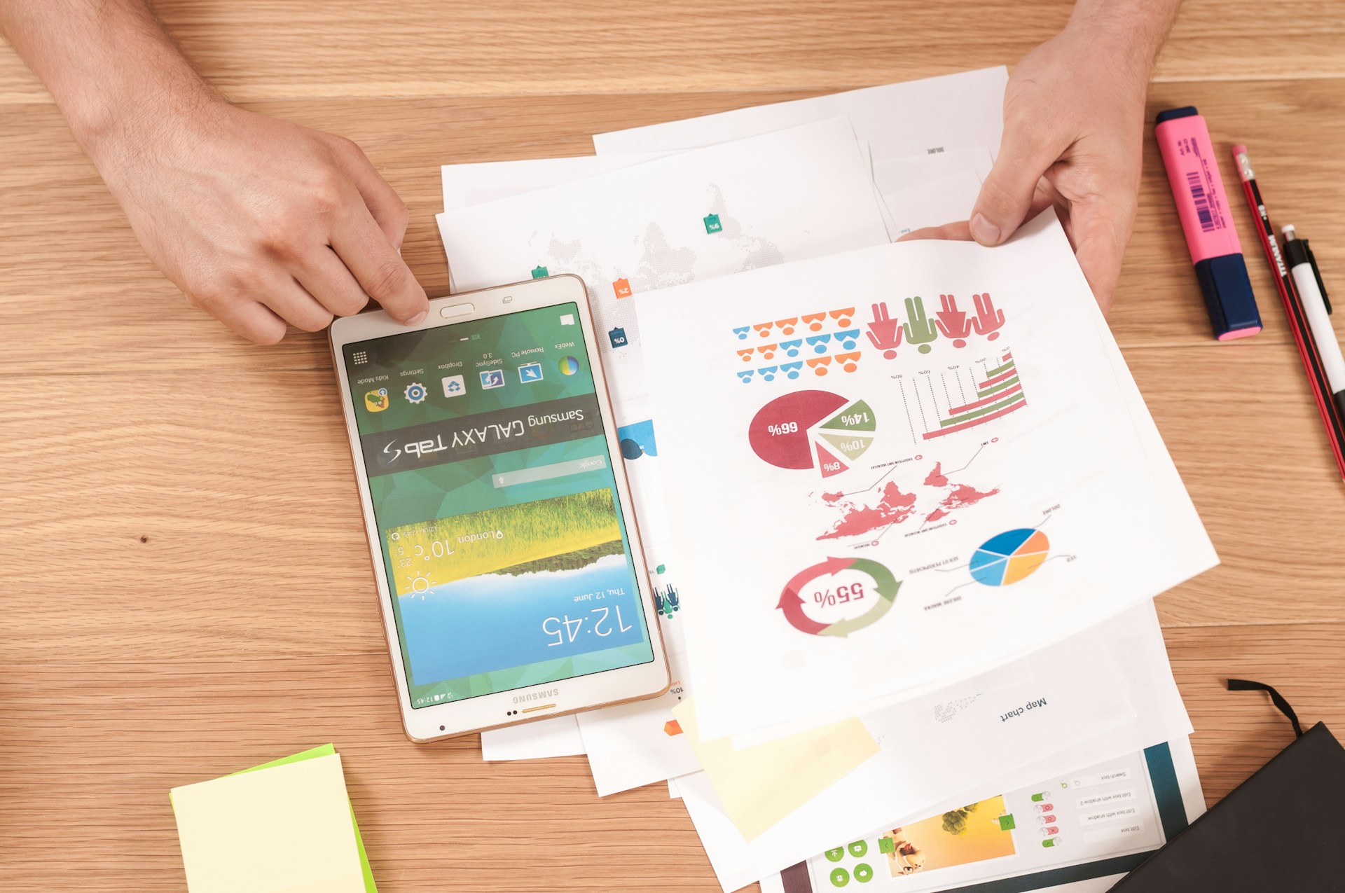 Hands with a tablet and printed charts and infographics on a desk