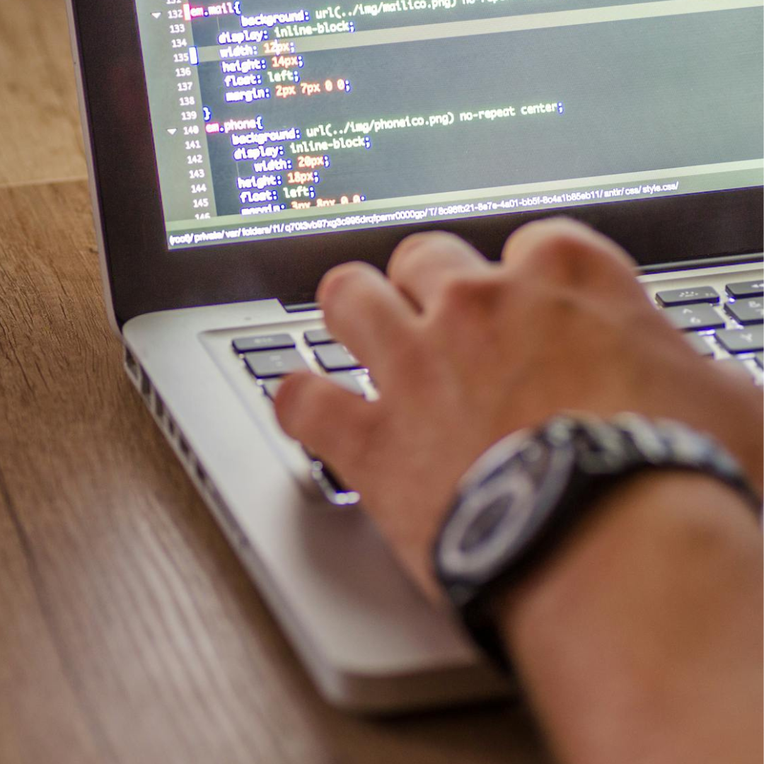 Hand typing on a laptop showing website code