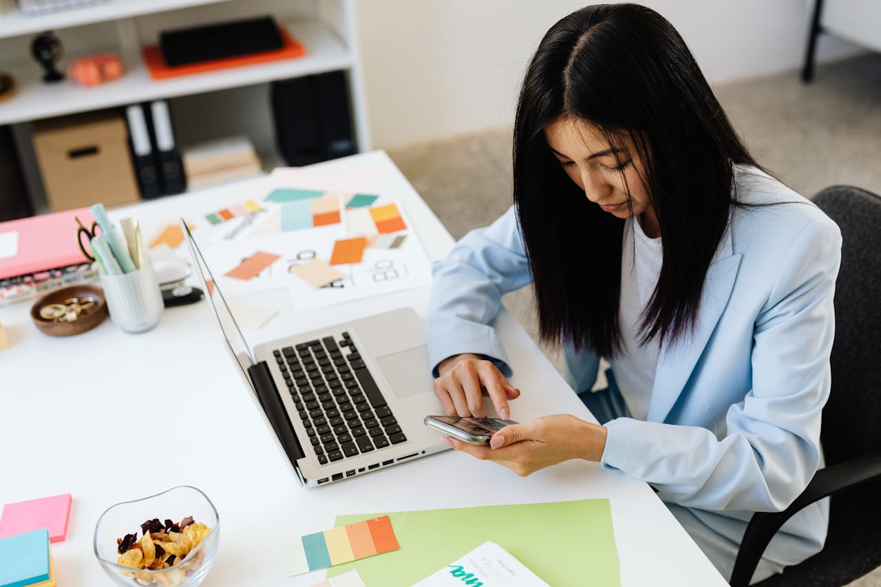Woman using her phone at a desk with a laptop and colour swatches